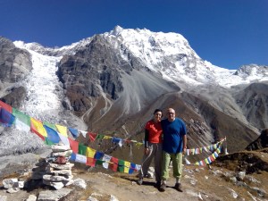 Pareja sonriendo frente a montañas nevadas y banderas de oración tibetanas en el fondo.