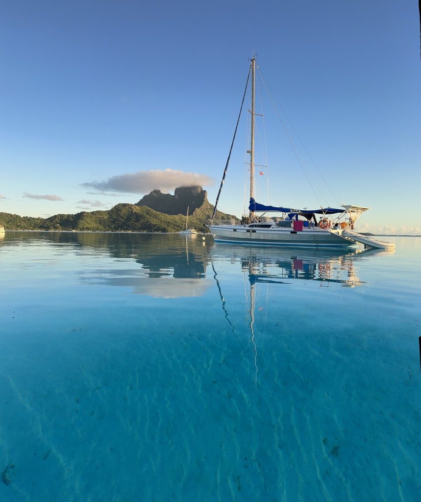 Un velero en aguas tranquilas y cristalinas, con montañas al fondo y un cielo despejado.