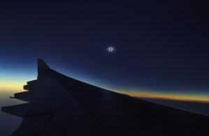 Vista nocturna desde un avión con el ala visible y un eclipse solar en el cielo.